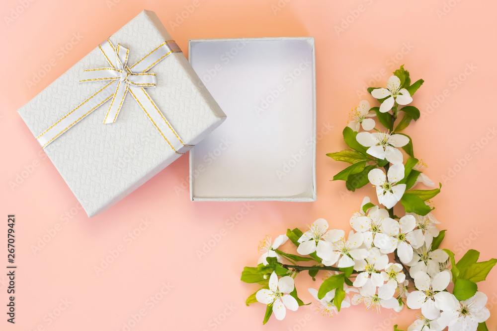 Open empty gift box with ribbon and spring flowers on pink background.