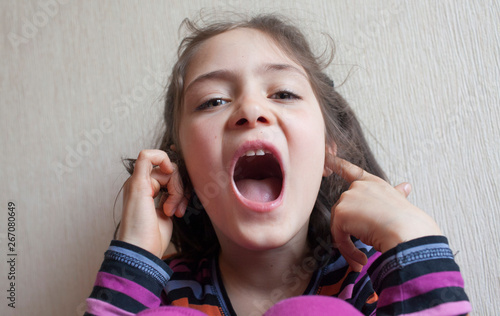 Little girl covers her ears with her hands and screams