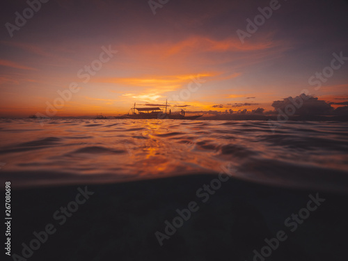 Red sunset at sea, boats with people over the water and water surface underwater.