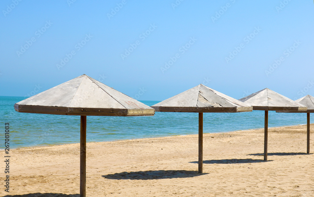 Beautiful empty beach. Sea coast with wooden umbrella and blue sky. The calm sea on a summer day in a tourism and vacation concept. 