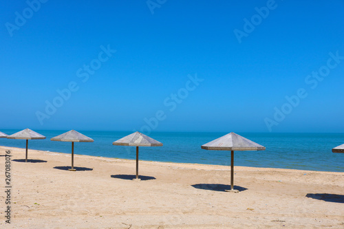Beautiful empty beach. Sea coast with wooden umbrella and blue sky. The calm sea on a summer day in a tourism and vacation concept. 