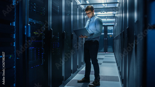 Foto In Data Center IT Engineer Stands Before Working Server Rack Doing Routine Maintenance Check and Diagnostics Using Laptop