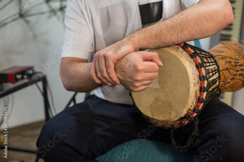 Musician having wrist pain while playing djembe drum instrument in home music studio.