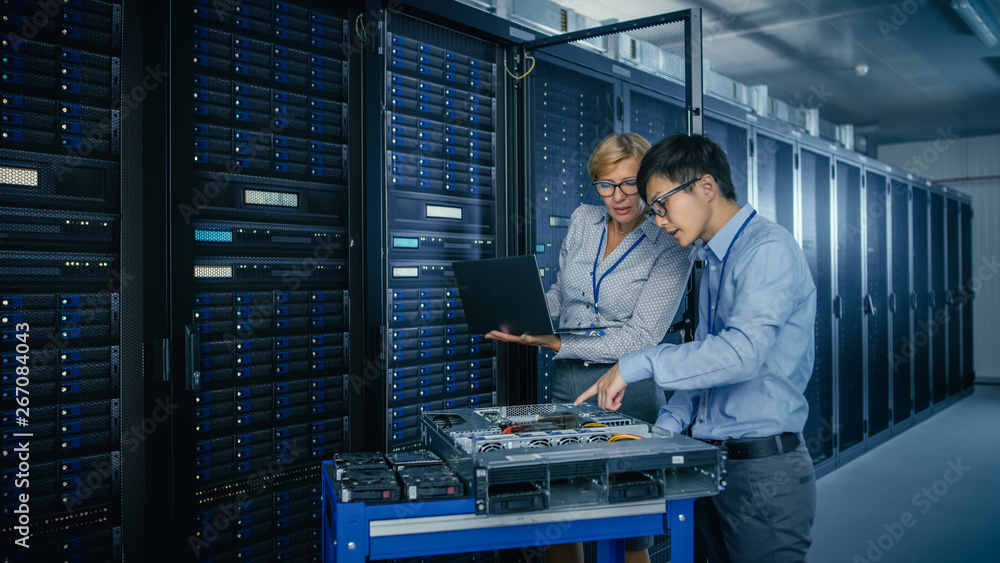Fototapeta premium In the Modern Data Center: Engineer and IT Specialist Work with Server Racks, on a Pushcart Equipment for Installing New Hardware. Specialists Doing Maintenance and Diagnostics of the Database.