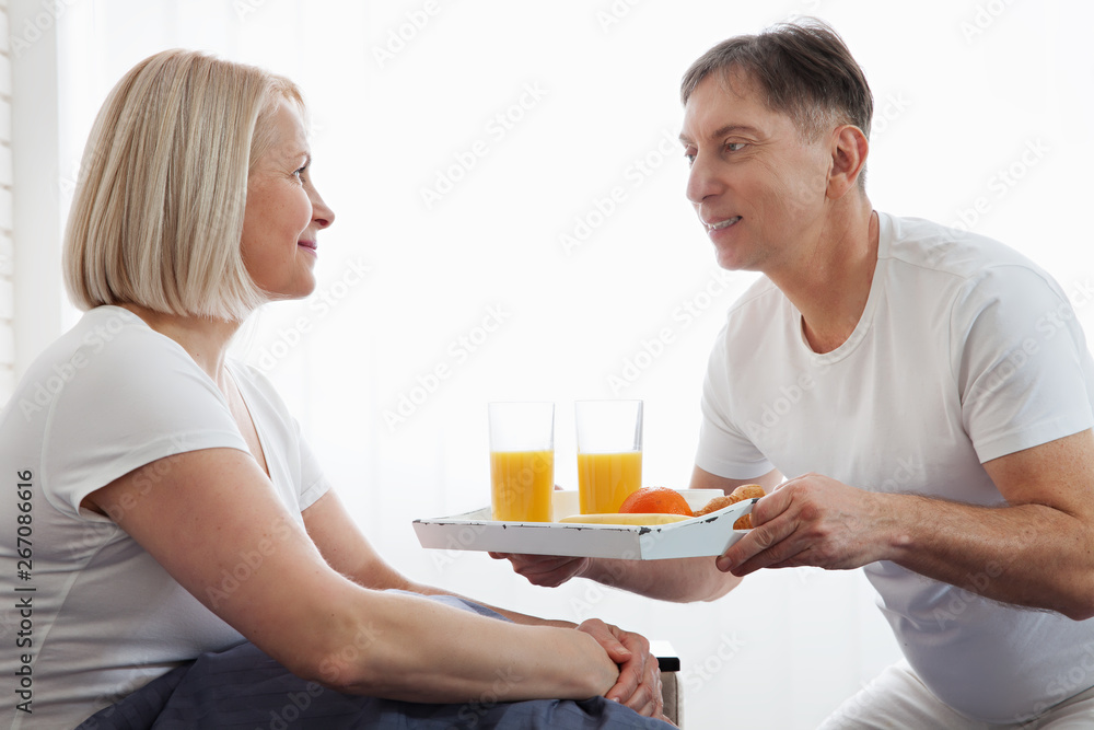 Beautiful couple having breakfast lying in bed at home. Handsome man and attractive woman are enjoying spending time together while gently hugging and kissing sitting in bed. Beautiful couple having breakfast lying in bed at home. Handsome man and attractive woman are enjoying spending time together while gently hugging and kissing sitting in bed.