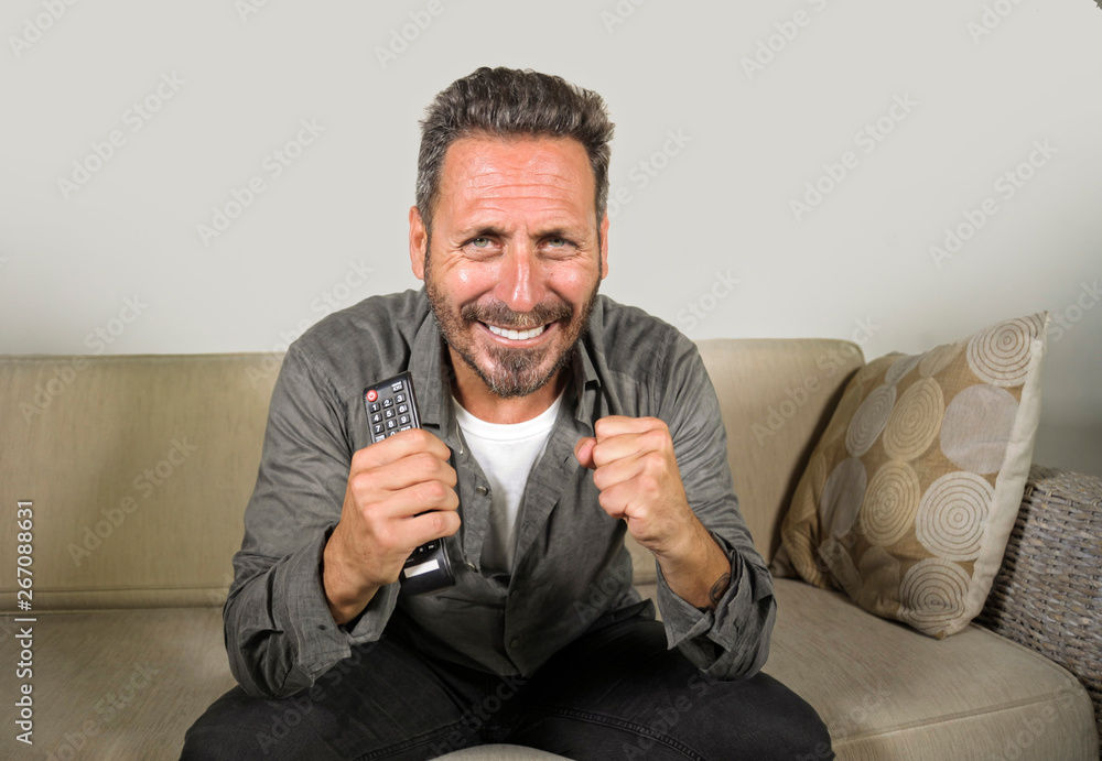 excited and attractive man on his 30s or 40s enjoying at home watching sport match or thriller movie on television feeling nervous sitting at living room sofa couch excited and attractive man on his 30s or 40s enjoying at home watching sport match or thriller movie on television feeling nervous sitting at living room sofa couch