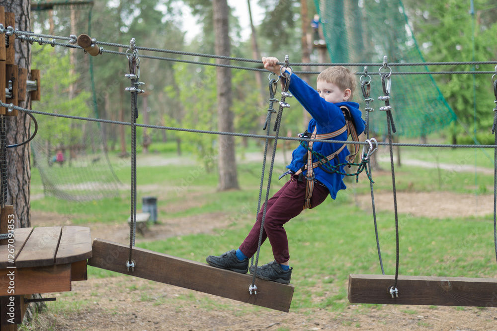 A little boy is training in a rope park. The child climbs the obstacle course. Active recreation in the park in the fresh air. A little boy is training in a rope park. The child climbs the obstacle course. Active recreation in the park in the fresh air.