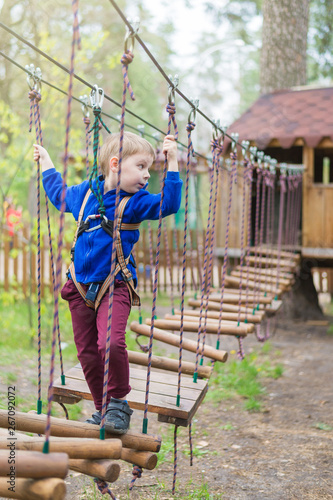 A little boy is training in a rope park. The child climbs the obstacle course. Active recreation in the park in the fresh air.