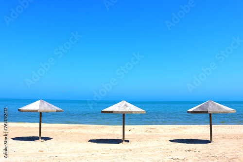 Beautiful empty beach. Sea coast with wooden umbrella and blue sky. The calm sea on a summer day in a tourism and vacation concept. 