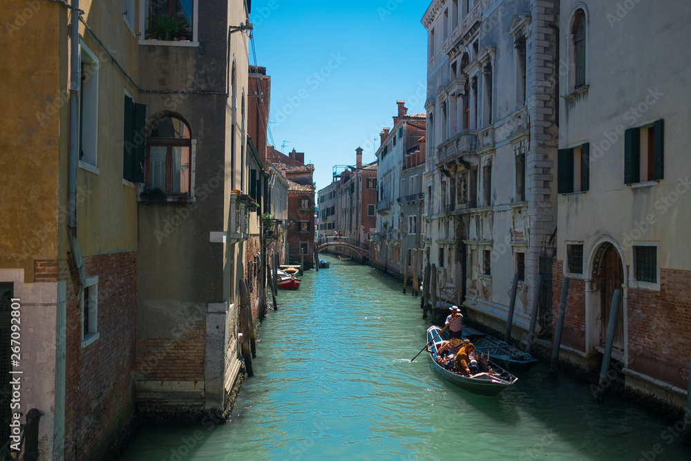 view of traditional venetian gondola boat in water canal with couple of lovers taking a romantic and relaxing ride during a sunny summer day