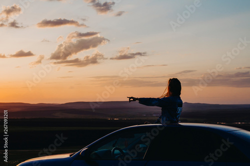 Silhouette of a woman at sunset who travels by car, a woman looks out of the car and shows her hand to the side