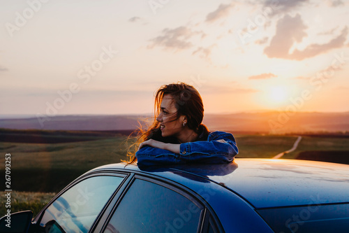 Woman standing leaning on the car at sunset