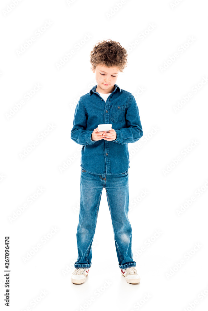 full length view of concentrated kid in denim clothes using smartphone isolated on white full length view of concentrated kid in denim clothes using smartphone isolated on white