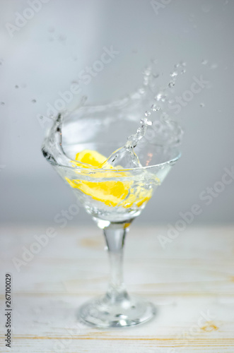 Martini glass with lemon slice splash on light background