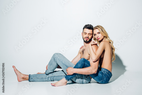 attractive blonde girl hugging shirtless boyfriend while sitting on white