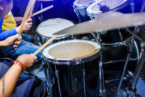 hands of teacher with wooden drumsticks guiding boy in drum learning tutorial in recording studio at music academy