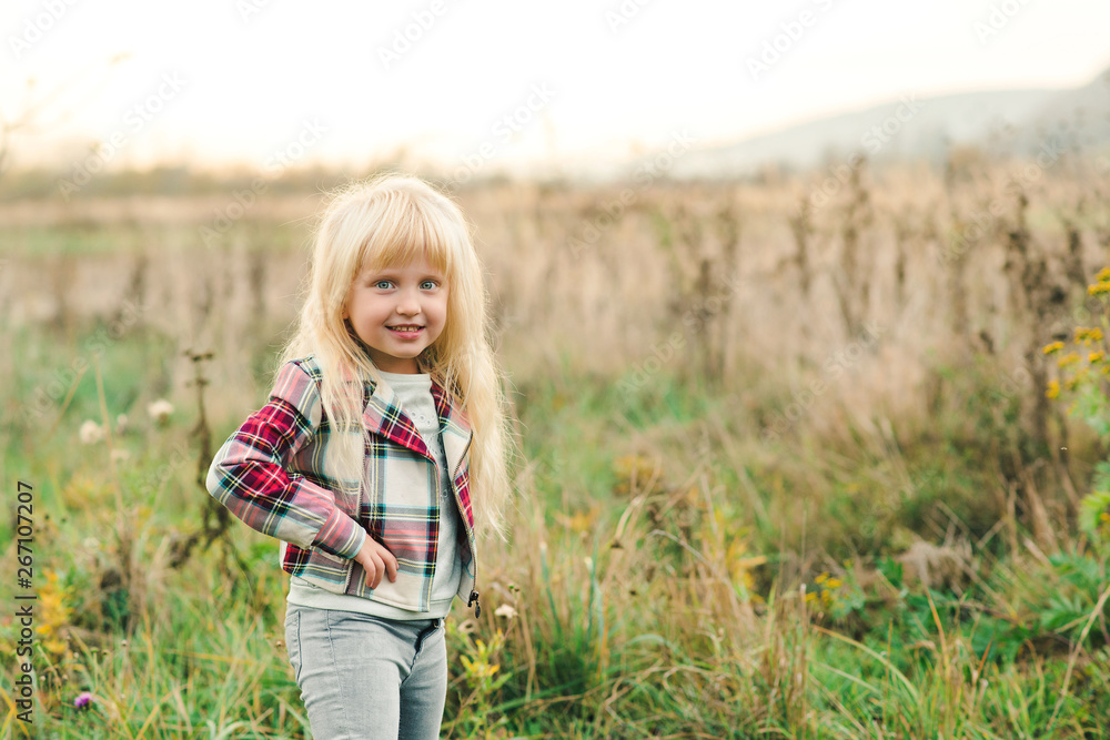 Cute little girl with long blonde hair and amazing eyes on nature background. Fashion stylish child outdoors. Happy and healthy childhood.