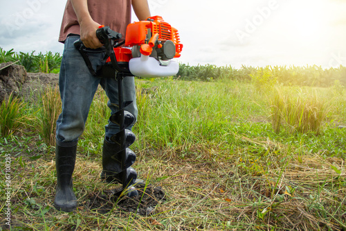 Schilderij op canvas farmer using tools hand-held soil hole drilling machine or portable manual earth auger for prepare the soil for planting trees with garden background organic farming and copy space