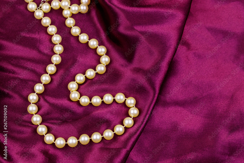 Pearl necklace on purple satin fabric background