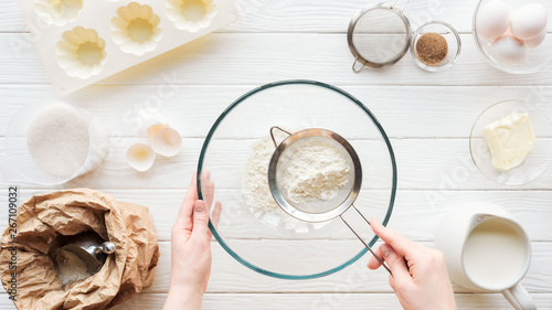cropped view of woman sieving flour in bowl on table with ingredients
