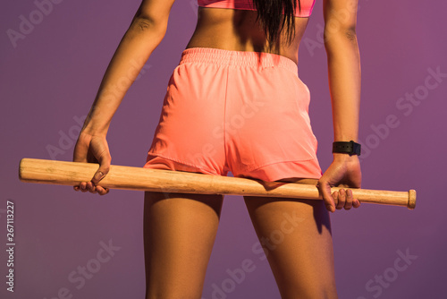 back view of sportive woman in yellow short holding baseball bat isolated on purple photo