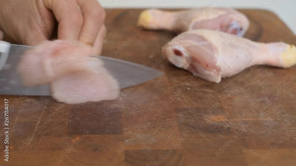 Close-up of a butcher cutting a chicken drumstick on a wooden board Close-up of a butcher cutting a chicken drumstick on a wooden board