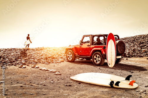 Red summer car on beach and free space for your decoration. Sunset time and surfer. 