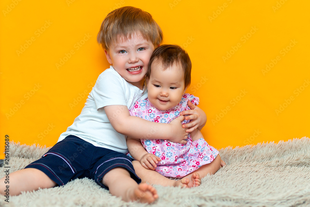 older brother hugging his little sister. Children in on a yellow background older brother hugging his little sister. Children in on a yellow background