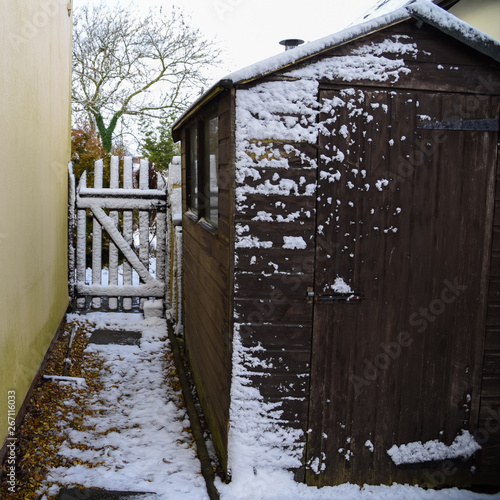 Garden path next to shed leading to wooden gate with a light covering of winter snow.