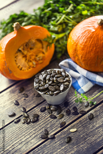 Roasted pumpkin seeds with raw pumpkins on wooden table