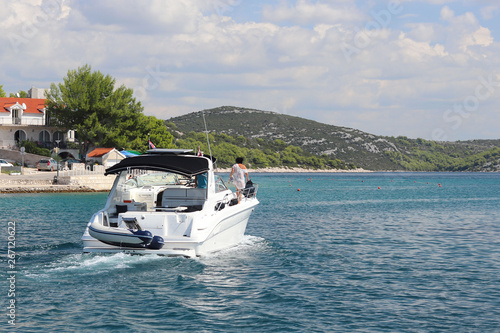 The company of friends on a small motor yacht sails along the coast near a small Mediterranean town. Rest on the water in the paradise. Cruise on a charter boat in the Croatian Riviera. Dalmatian isla