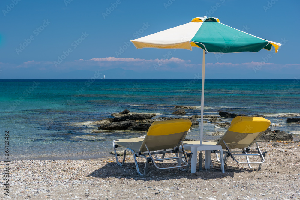 Sun beds, lounge chairs and an umbrella on the beach, on the seashore.