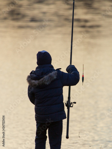 The boy catches fish on the pond at sunset