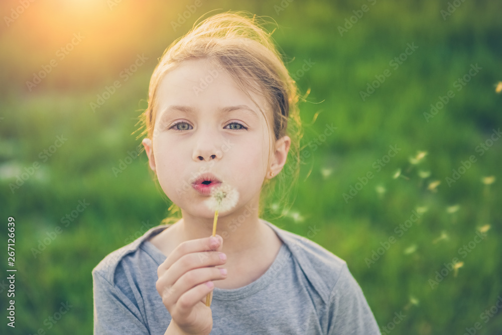 Happy child blowing dandelion flower outdoors. Girl having fun in spring park. Blurred green background. Dream and imagination concept Happy child blowing dandelion flower outdoors. Girl having fun in spring park. Blurred green background. Dream and imagination concept