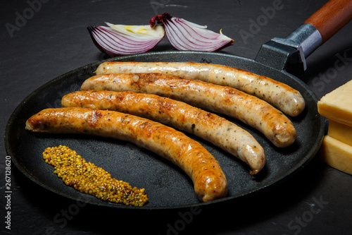 big frying pan with fried thin sausages and granular mustard