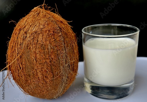 coconut milk with a big brown nut next to a black background