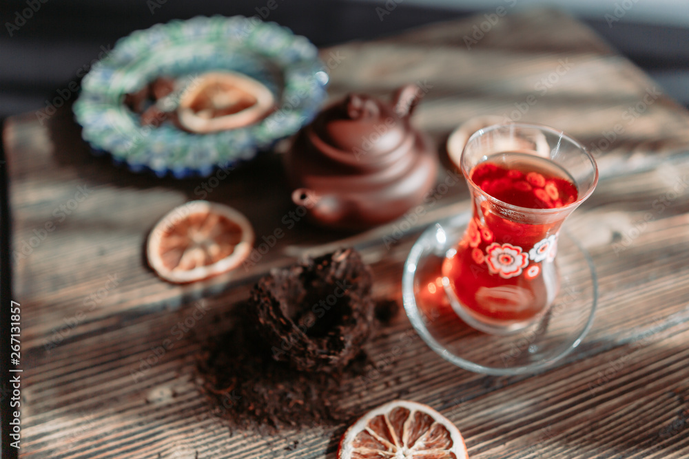 Black tea in traditional turkish tea cup with pattern on wooden table, traditional clay teapot with Puer tea, orange chips near on wooden table. Shallow focus. Horizontal image. Black tea in traditional turkish tea cup with pattern on wooden table, traditional clay teapot with Puer tea, orange chips near on wooden table. Shallow focus. Horizontal image.