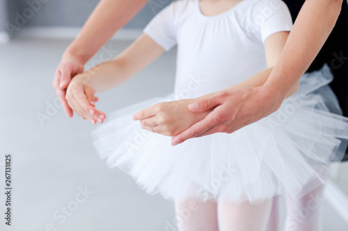 Ballet teacher helps little ballerina in classical dance school. Female dance trainer is teaching kid girl to do choreographic position with hands. Practicing for children. Close up.
