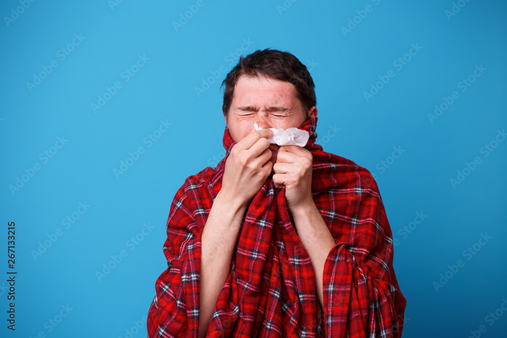 A wrapped in a blanket sick man is blowing his nose in white handkerchief A wrapped in a blanket sick man is blowing his nose in white handkerchief