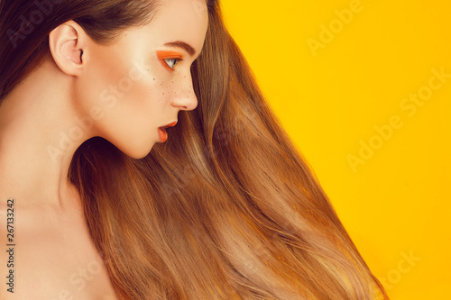 Beautiful model girl with shiny brown and straight long hair . Keratin straightening . Treatment, care and spa procedures. Smooth hairstyle. Woman with irange makeup with freckles. Empty space orange