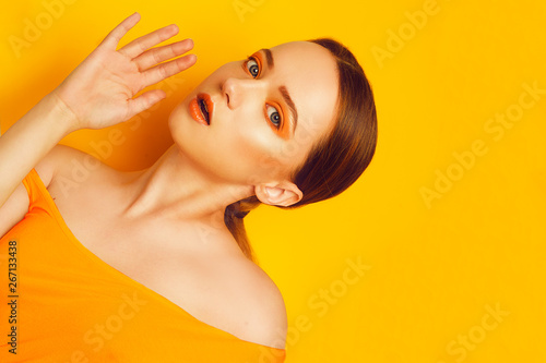Beauty Model Girl with yellow / orange professional makeup. Orange eye shadow and lipstick Fashion woman with long, straight hair. High fashion trend make up. Yellow / orange background. Fashion