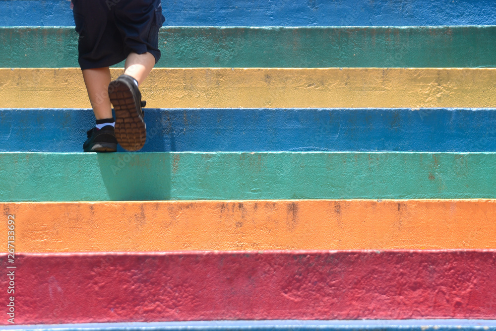 Lower part of a boy in casual shoe walking up outdoor colorful stair children lifestyle successful concept - obrazy, fototapety, plakaty 