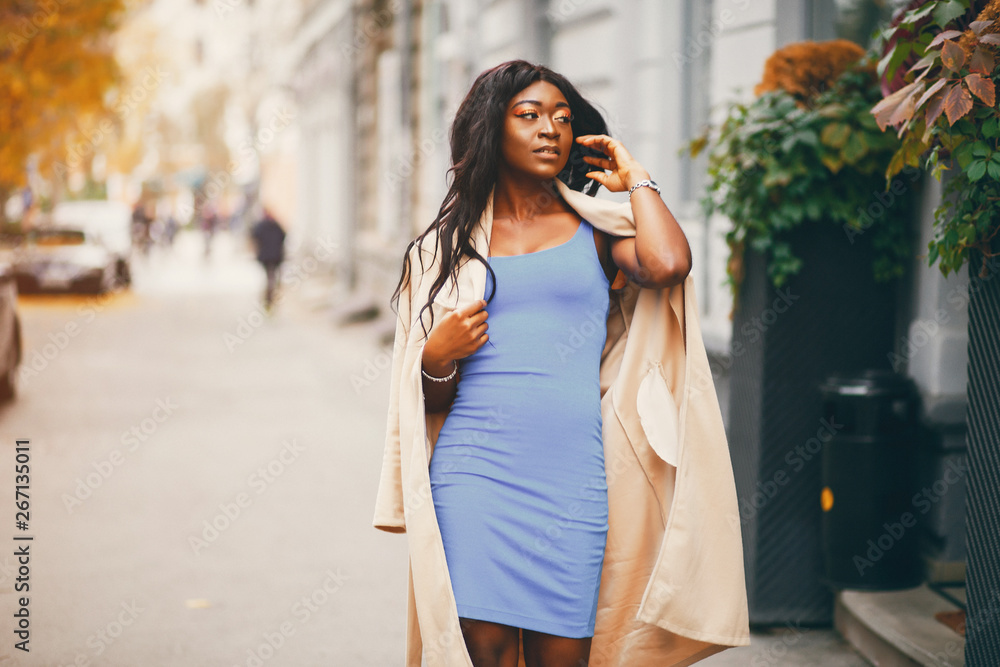 Elegant black woman standing in a autumn city. Businesswoman in a blue dress
