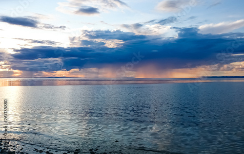 Sunset on Lake Baikal. Evening, rain, clouds, sun. Dramatic sky. Atmospheric landscape. The shore of Lake Baikal. Russia.