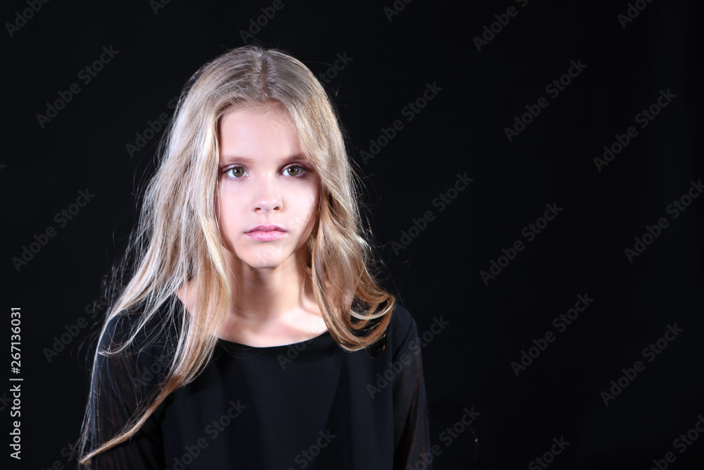 Portrait of a blonde girl with long hair on a black background. Emotional portrait.The girl shows different emotions on the face. Plays with long hair.