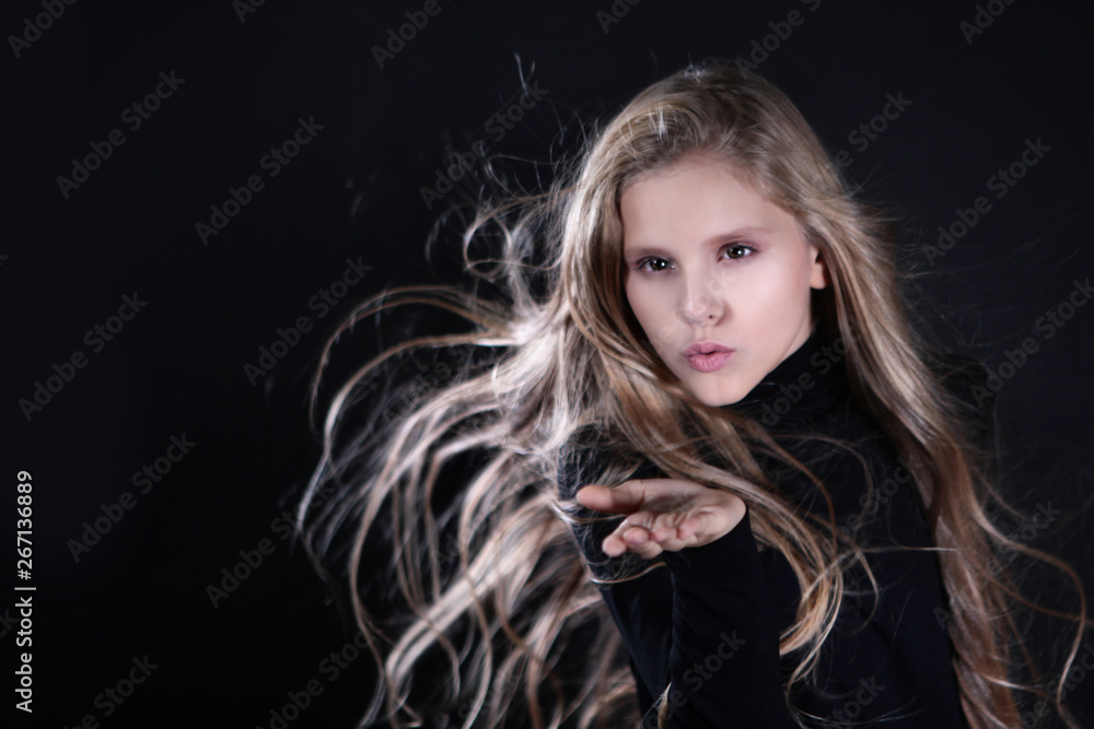 Portrait of a blonde girl with long hair on a black background. Emotional portrait.The girl shows different emotions on the face. Plays with long hair. Portrait of a blonde girl with long hair on a black background. Emotional portrait.The girl shows different emotions on the face. Plays with long hair.