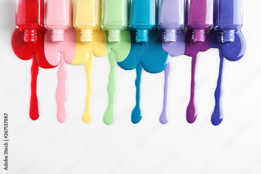 Spilled colorful nail polishes and bottles on white background, top view