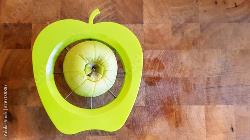 A green apple being separated into chunks by a green apple shaped slicer, divider and corer on a wooden butchers block.