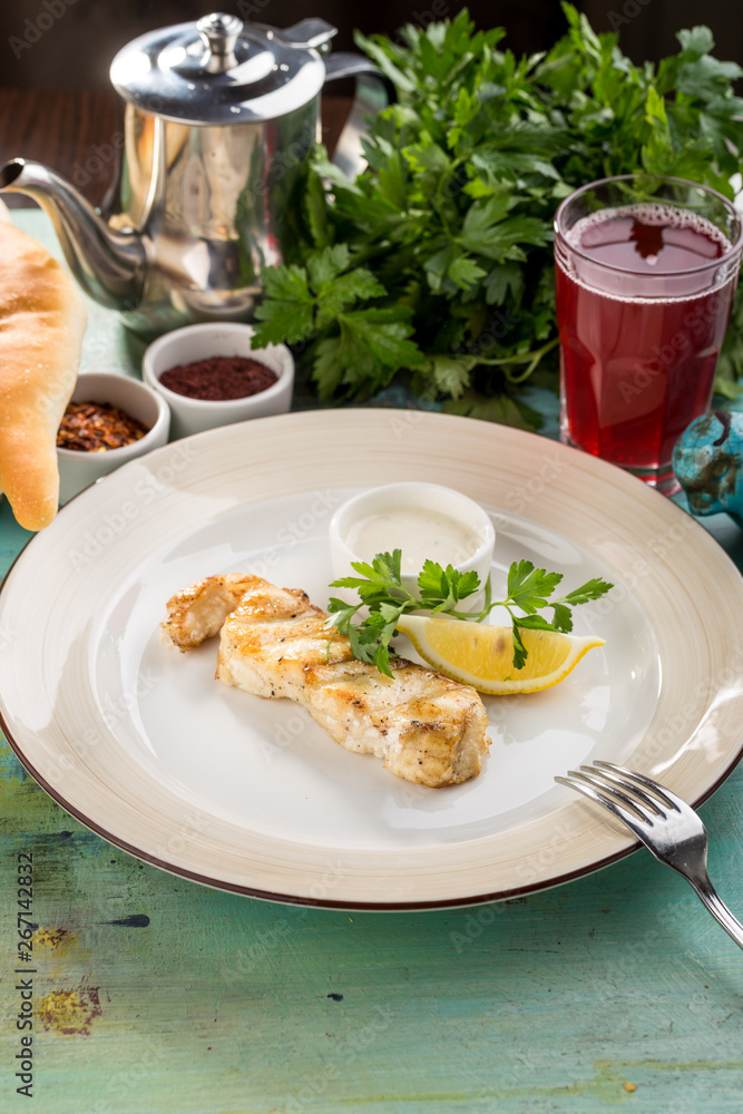 White fish fillet baked with lemon slice and white sauce on blue wooden table White fish fillet baked with lemon slice and white sauce on blue wooden table