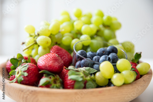 Wooden bowl with fruits: strawberries, blueberries and green grapes.